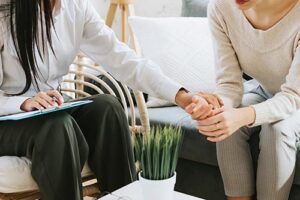 two people are sitting and one person holds the hand of the other person while trying to comfort them in their anxiety treatment