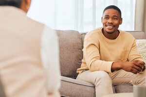 a smiling man sits on a couch and discusses substance use treatment with his therapist